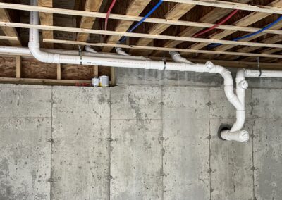 Basement Under Construction With Network Of Plumbing Pipes Hanging From The Ceiling.